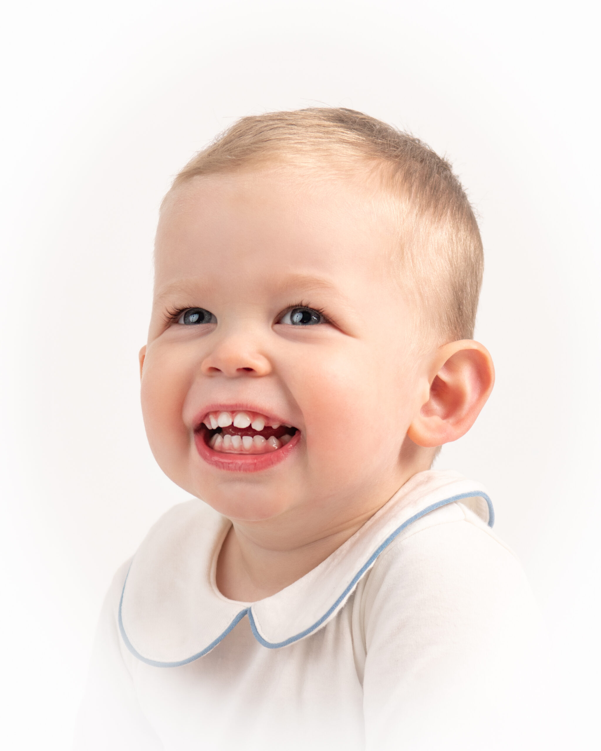 One year old boy smiling generously for a portrait in studio.